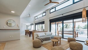 Un vaste espace de vie comprenant un grand lit, une table basse ronde et des poufs en fibres tressées.
