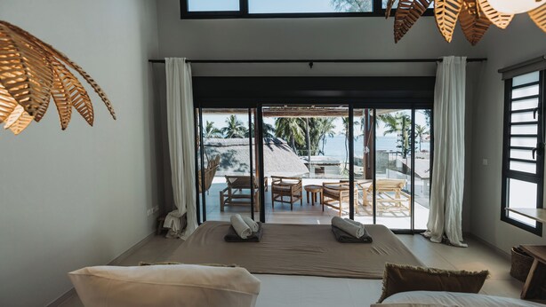 Une chambre dotée d’un grand lit, donnant sur une piscine, et équipée d’un ventilateur de plafond.