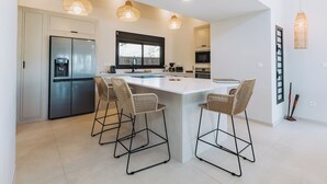 Une cuisine moderne dotée d’un îlot central, de tabourets de bar, d’un réfrigérateur et de luminaires suspendus.