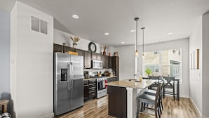 A modern kitchen with stainless steel appliances, a central island, and a dining area with wooden chairs. - Awesome Balcony | Near Denver & Boulder (Broomfield)
