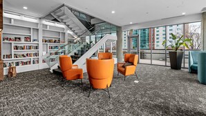 Eine moderne Bibliothek mit Treppe, Bücherregalen, orangefarbenen Sesseln und großen Fenstern.