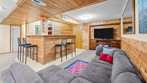 A cozy cabin interior with a wooden bar area, a TV, and a large gray sofa. - New! Recently Updated- Near Parks & Rec Center, Fenced Yard- 30 Day Rental (Littleton)