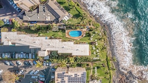 Luftaufnahme eines Küstenhotels mit Schwimmbad, Parkplatz und Meerblick.