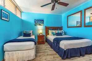 A room with two beds, a ceiling fan, a wooden nightstand with a lamp, and a large mirror on the wall. - Stunning Ocean View Gem with AC: Kamaole Nalu 504 - Your Island Getaway! (Kihei, Maui)