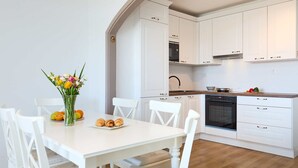 A modern kitchen with white cabinetry, a built-in oven, and a dining area with a white table and chairs. - Hedera A9 (Dubrovnik)