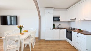 A modern kitchen with white cabinetry, a wooden countertop, and a built-in oven. There is a dining table with chairs and a vase of flowers. - Hedera A9 (Dubrovnik)