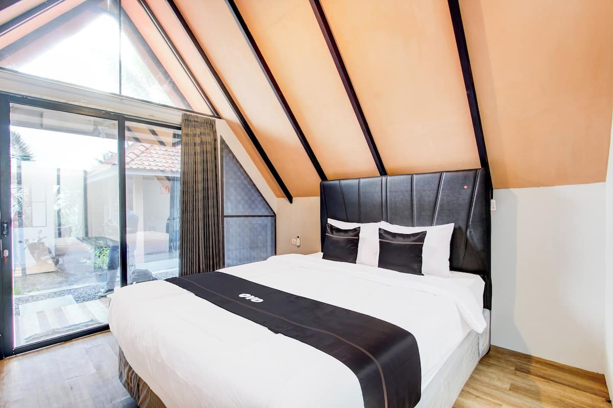 Ein modernes Schlafzimmer mit einem großen Bett, einer Schiebetür zu einem Außenbereich und einer geneigten Decke.