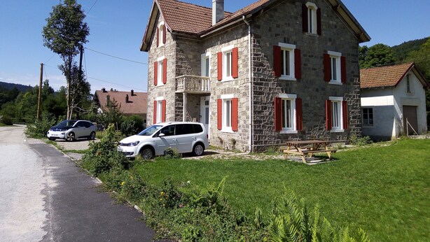 A two-story stone house with red shutters, a paved driveway, and a grassy lawn. - Nouveau Loft à Moins de 100m du lac Classé 2 (Gérardmer)