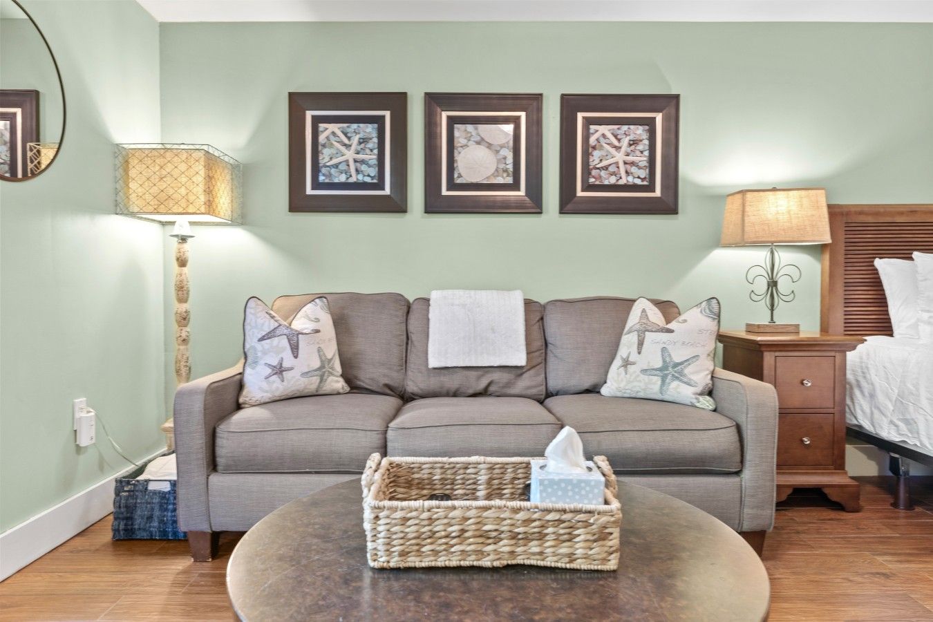 A room with a sofa, a bedside table, a lamp, and framed artwork on the wall.