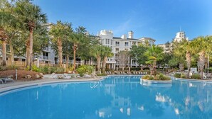 Ein Swimmingpool, umgeben von Palmen und einem Hotelgebäude mit mehreren Balkonen.