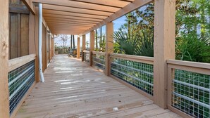 Eine Holzterrasse mit Geländer, überdacht und mit Blick auf Grünflächen.