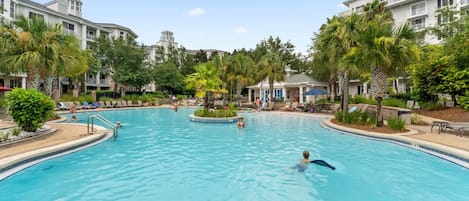 A large swimming pool with a central island, surrounded by lounge chairs and palm trees.