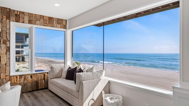 A modern living room with a large window overlooking a beach. - Oceanfront Oasis Retreat (Dana Point)