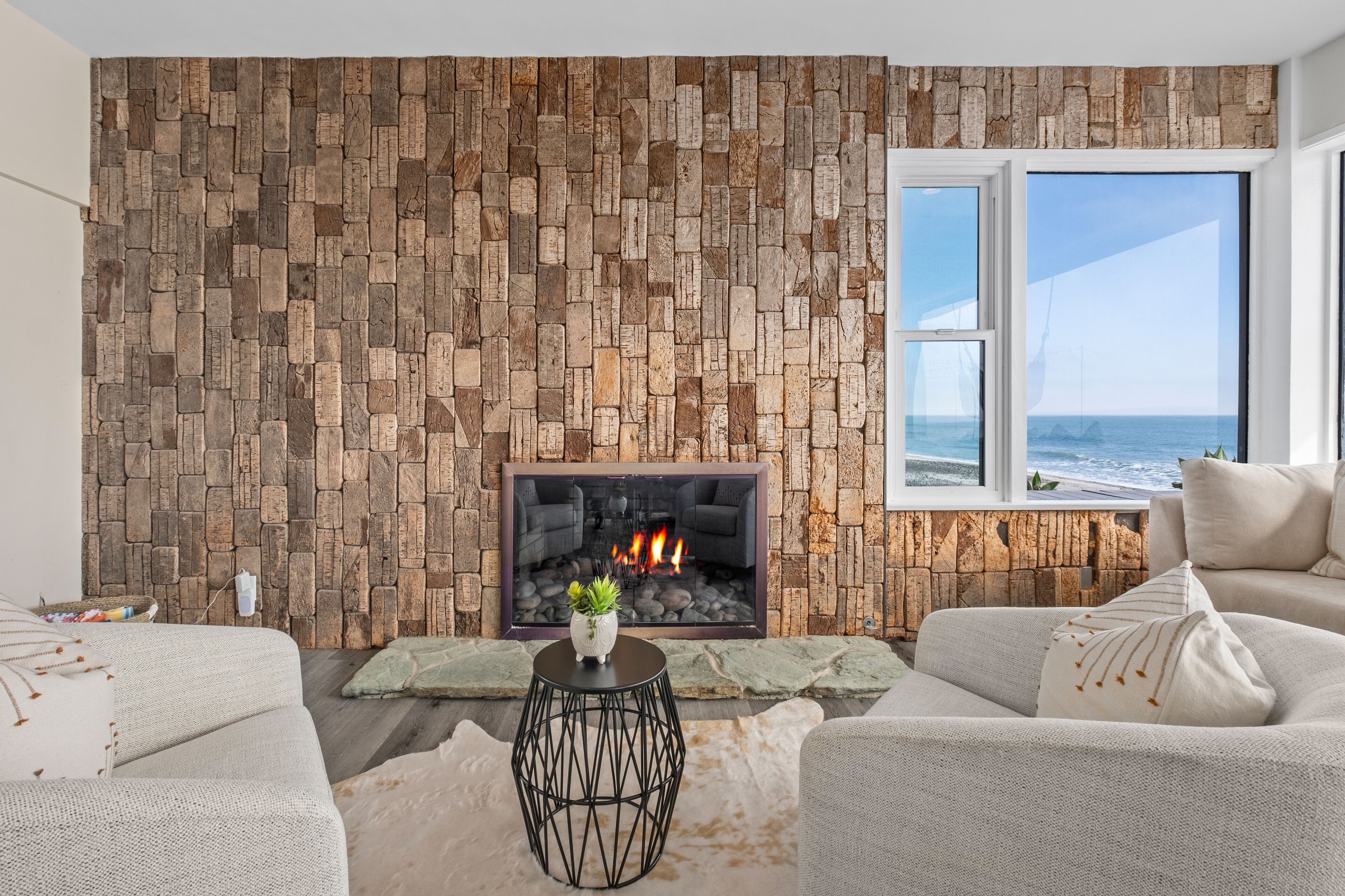 A living room with a stone wall, a fireplace, a view of the ocean, and a sofa.