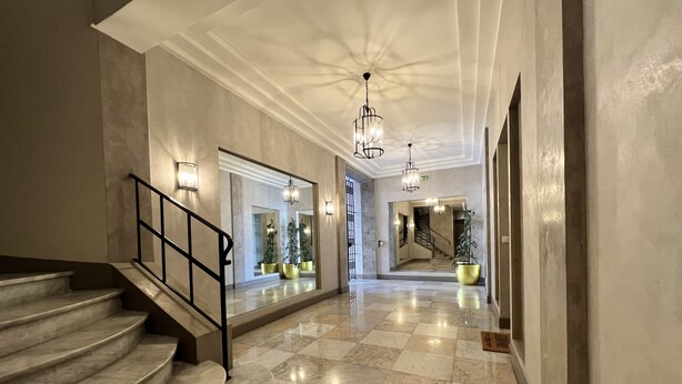 A marble-floored hallway with a staircase, wall sconces, and a large mirror reflecting the space. - FON3 (Cannes)
