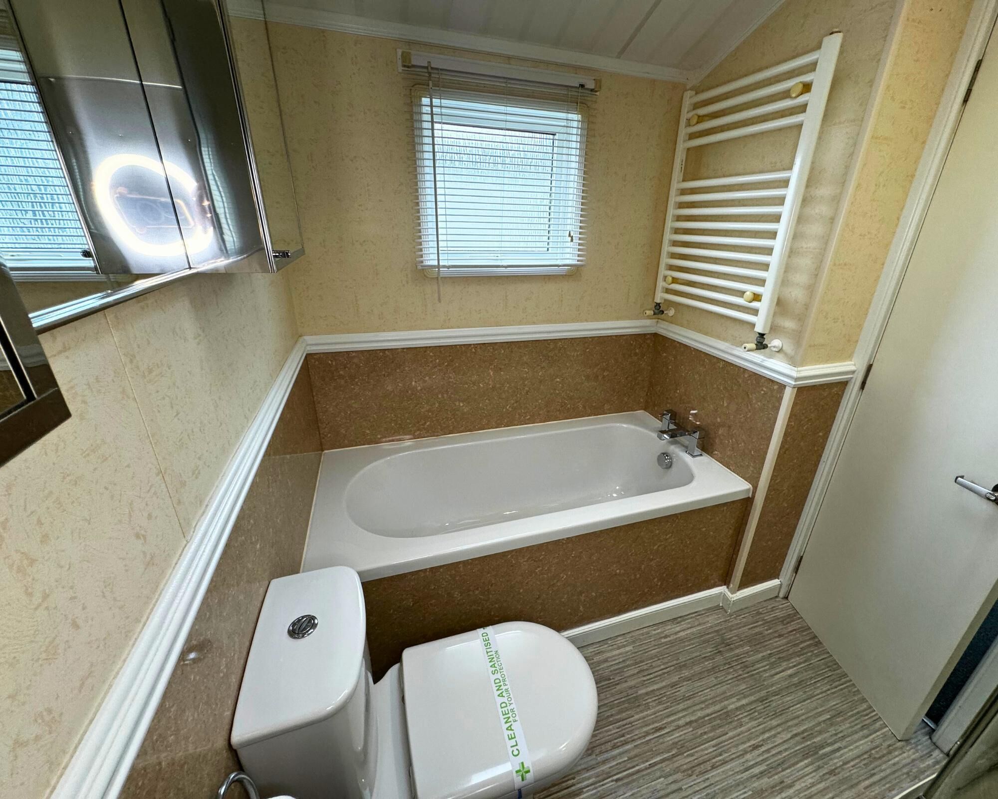 Une salle de bain avec une baignoire, des toilettes et une fenêtre avec des stores.