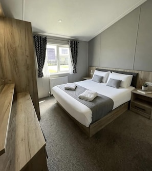 A modern hotel room with a large bed, bedside tables, a wooden desk, and a window with curtains.