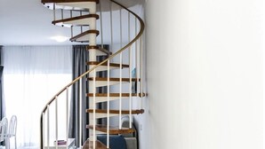 Un escalier en colimaçon moderne, avec des marches en bois et des rampes en métal, se trouve dans une pièce spacieuse et bien éclairée, dont le sol est recouvert de carreaux.