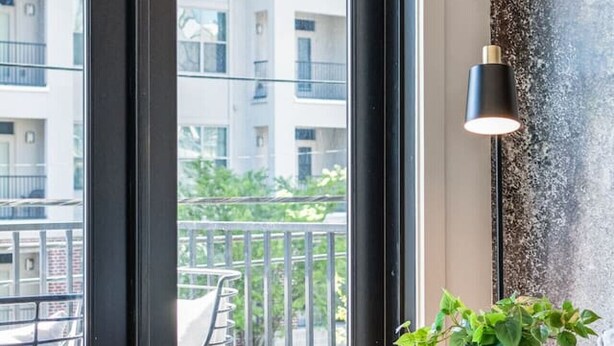 A modern room with a large window, a potted plant, and a lamp. - Comfortable Game-day condo near Vanderbilt with pool and game room (Nashville)