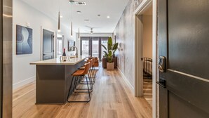 A modern kitchen with a central island, bar stools, and a large potted plant. - Comfortable Game-day condo near Vanderbilt with pool and game room (Nashville)