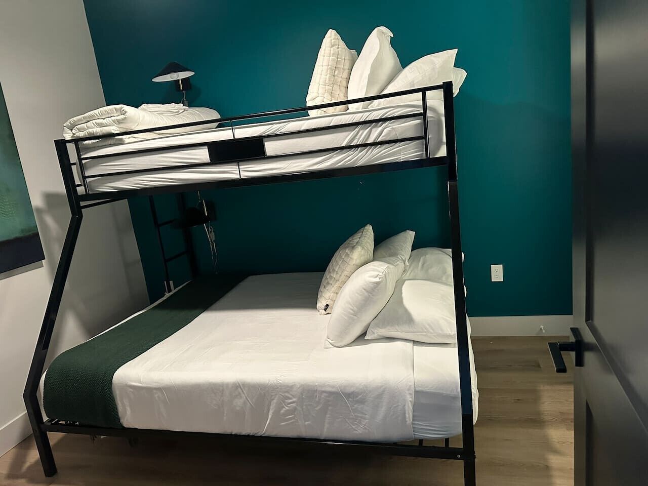 A bunk bed with white bedding and pillows, a green throw blanket, and a black metal frame.
