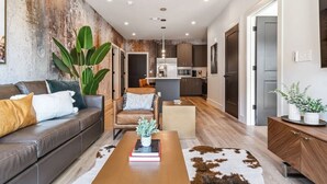 A modern living room with a leather sofa, a coffee table, and a large plant. - Comfortable Game-day condo near Vanderbilt with pool and game room (Nashville)