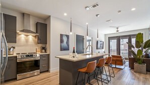 A modern kitchen with a central island, bar stools, and a dining area with a sofa. - Comfortable Game-day condo near Vanderbilt with pool and game room (Nashville)