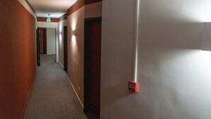 Pasillo de hotel con pisos alfombrados, paredes de madera y un letrero de salida de emergencia rojo.