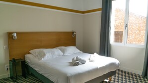 Una cama bien tendida con ropa de cama y toallas blancas, cabecera de madera y un estampado de cuadros en el suelo.