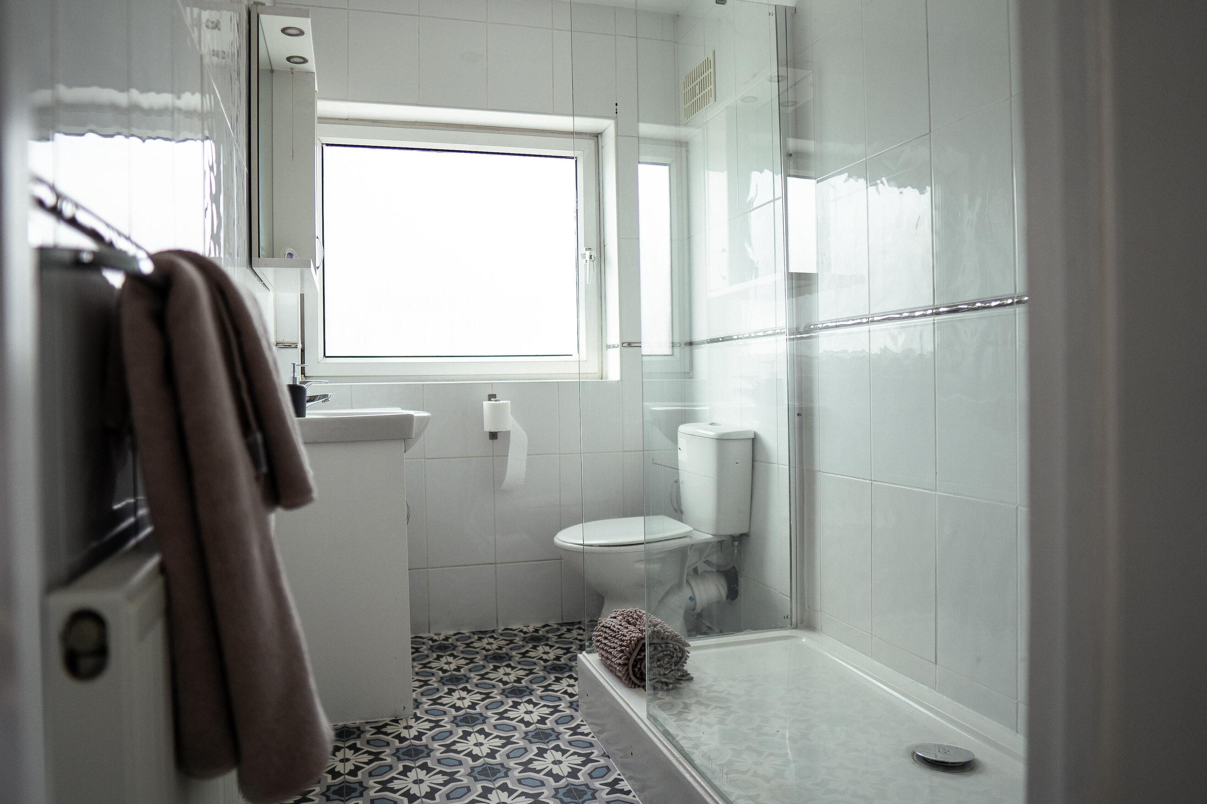 A bathroom with a toilet, a sink, a glass shower enclosure, and a patterned floor.