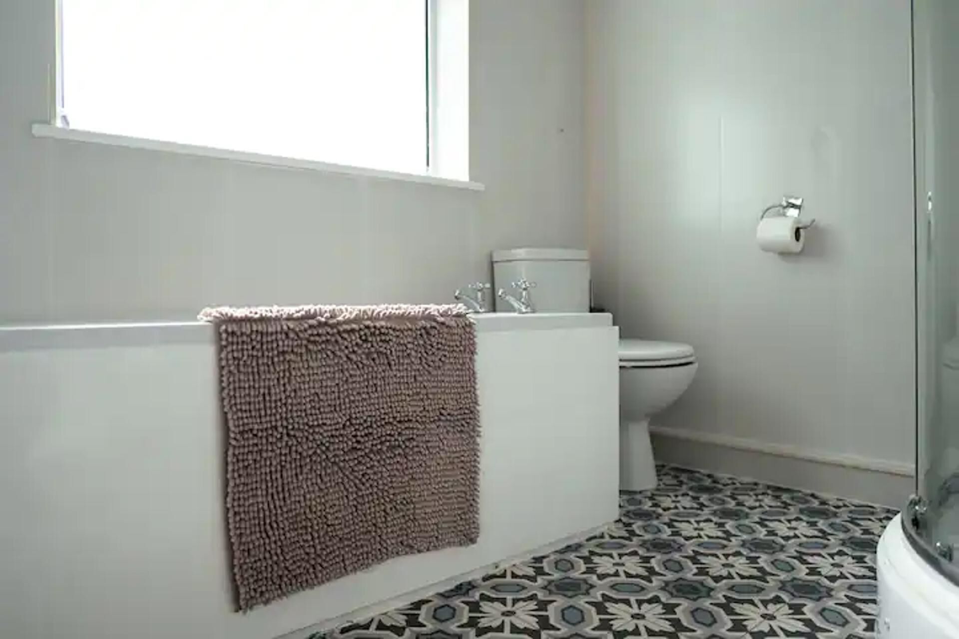 A bathroom with a bathtub, toilet, and patterned floor tiles.