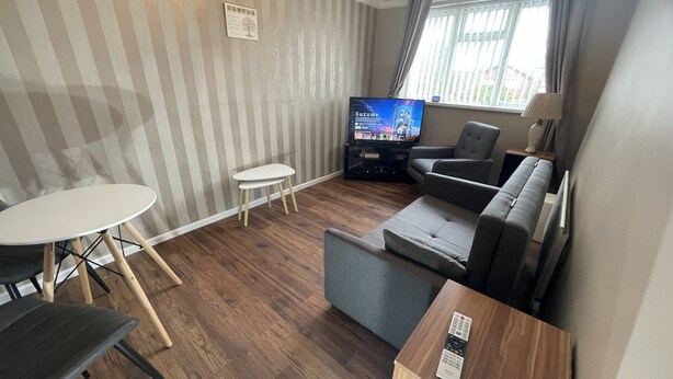 A living room with a flat-screen TV, grey sofa, a small round table, and a wooden coffee table. - Comfy One Bedroom Apartment  (Darlaston)