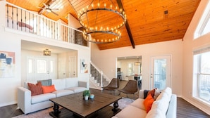 A spacious living area with a high ceiling, a staircase, and a view of the city.
