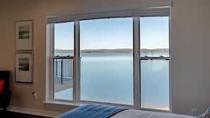 A bedroom with a large window overlooking a body of water, a bed, and two framed pictures on the wall.