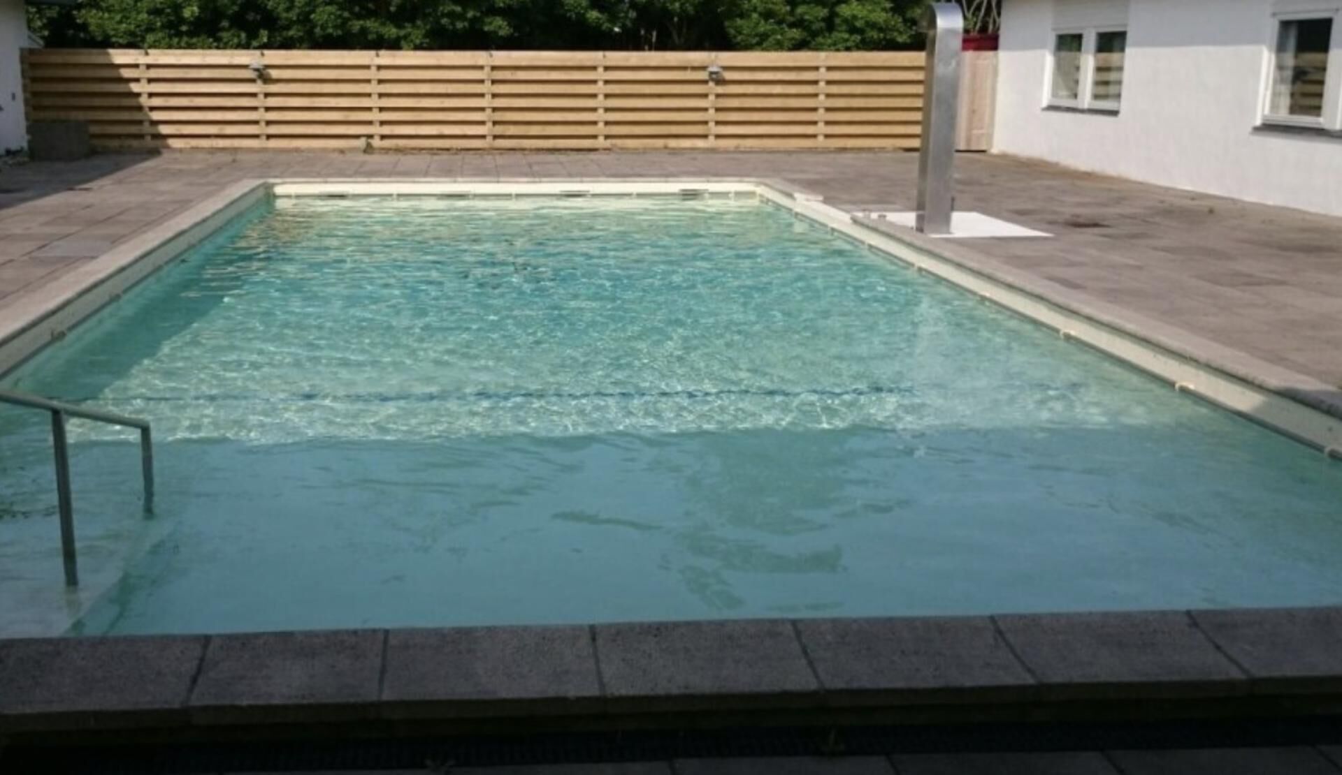 Una piscina rettangolare con una scala metallica su un lato, circondata da un solarium lastricato.