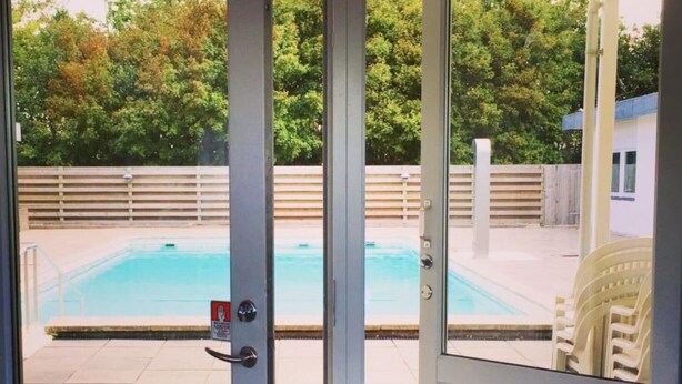 A view through a glass door of a swimming pool area with a wooden fence and chairs.