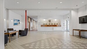 A spacious lobby with a reception desk, a seating area with a table and chairs, and a tiled floor.