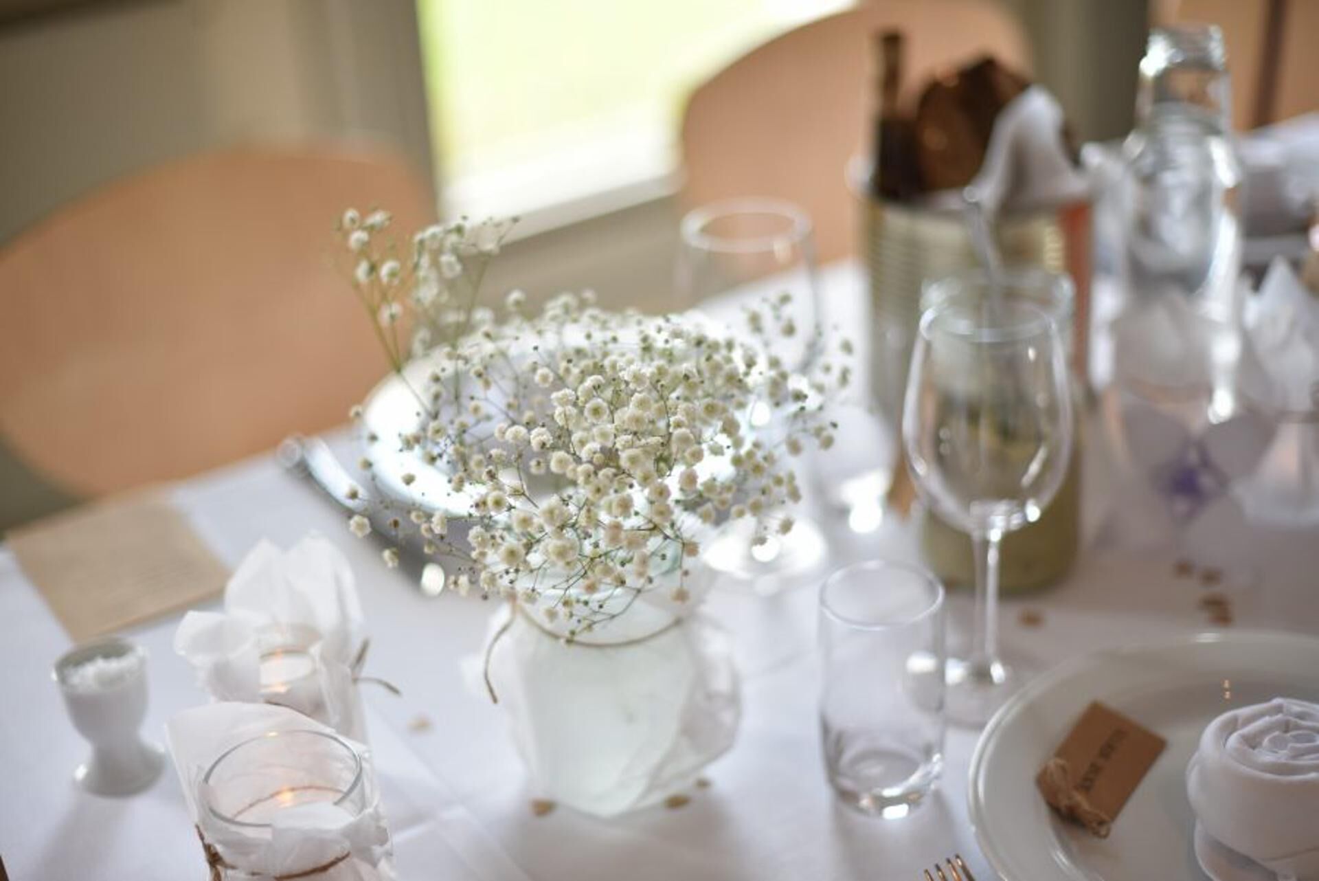 A table set with white tablecloth, clear glassware, and a centerpiece of white flowers.