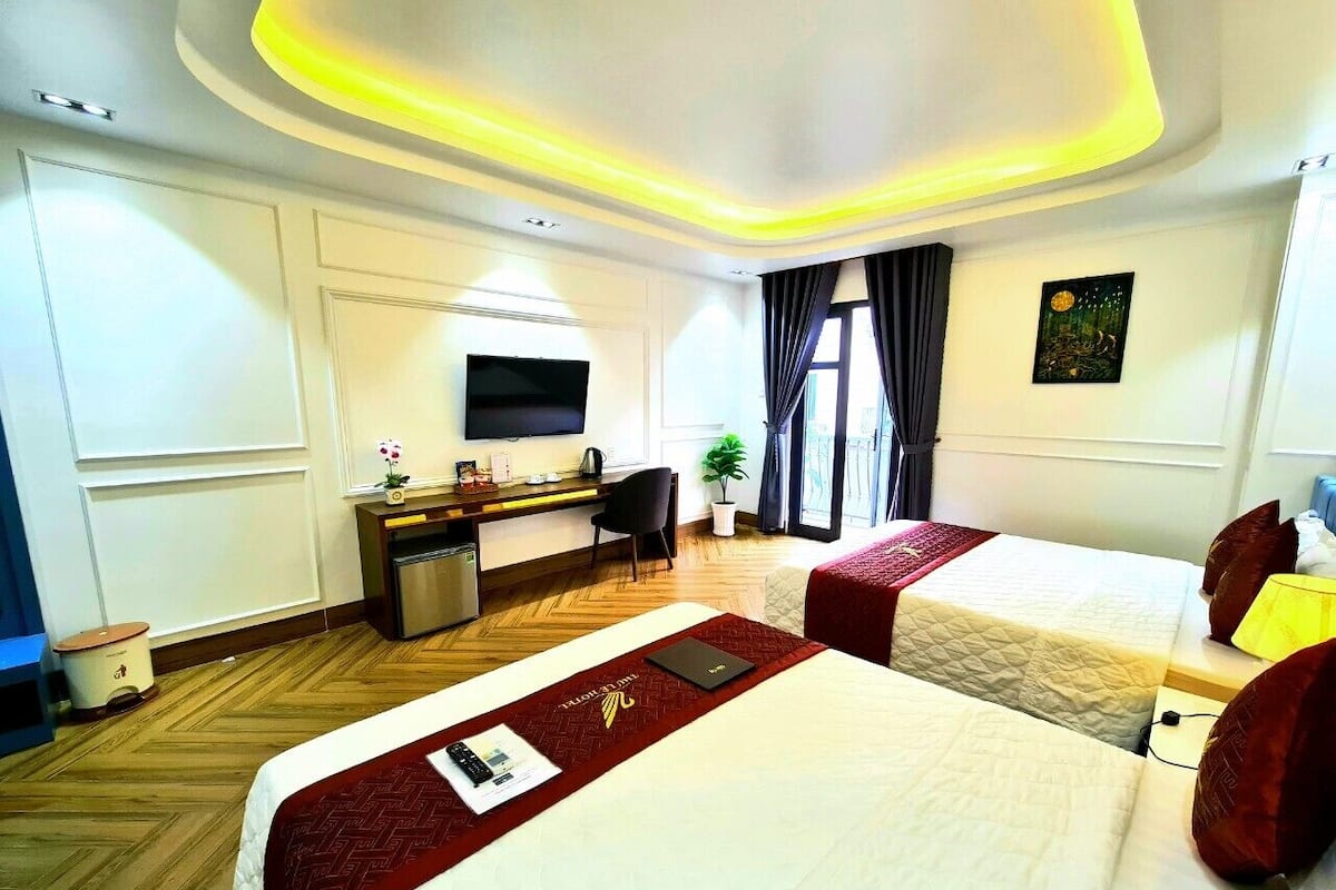 Quarto de hotel com duas camas, uma mesa, uma televisão e uma janela com cortinas.
