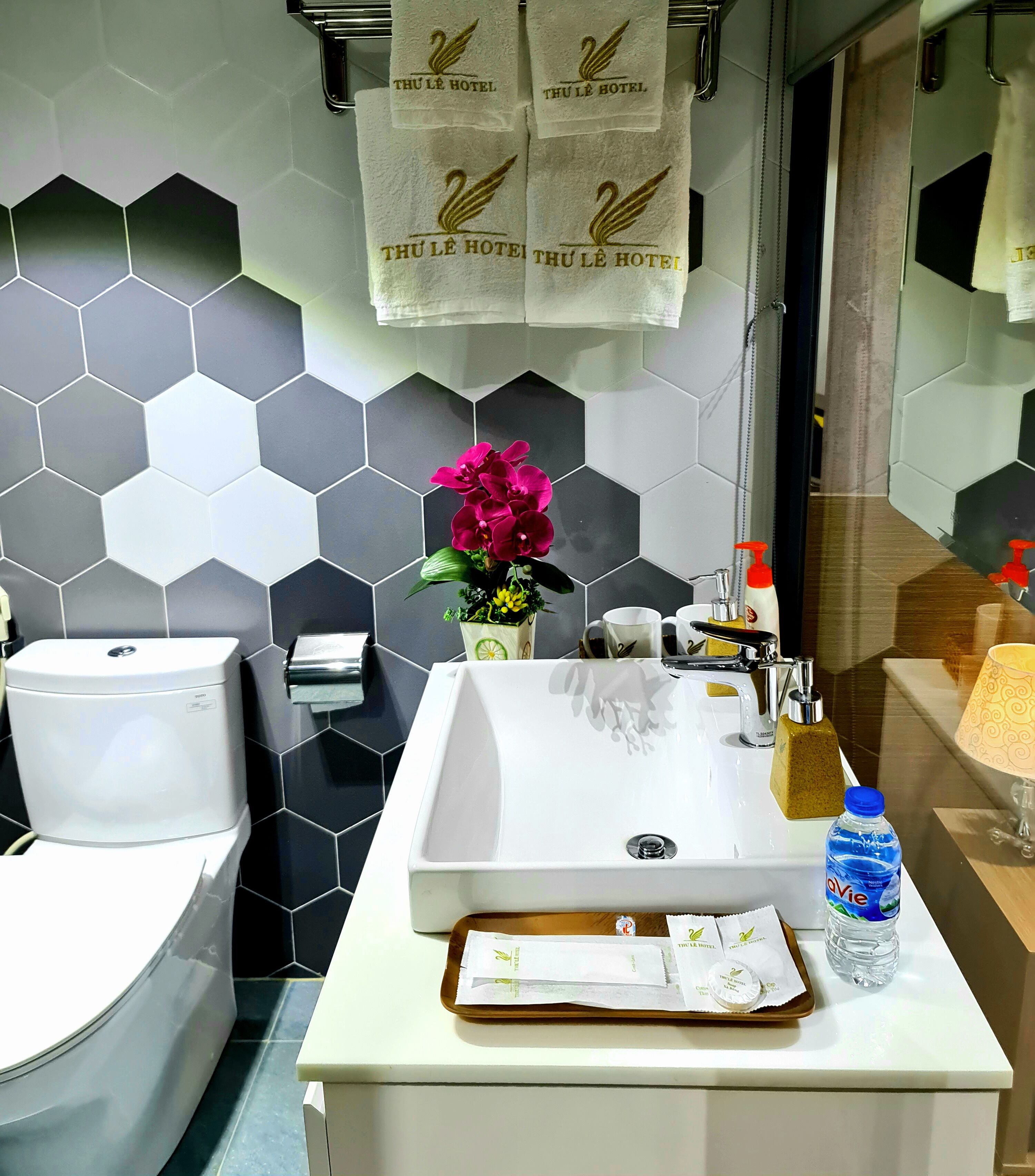 A bathroom with a toilet, sink, and shower. There are towels hanging on a rack, a potted plant, and toiletries on the sink counter.