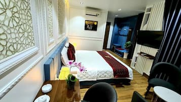Une chambre d’hôtel comprenant un lit, un bureau avec une chaise, une petite table avec un vase et un téléviseur.