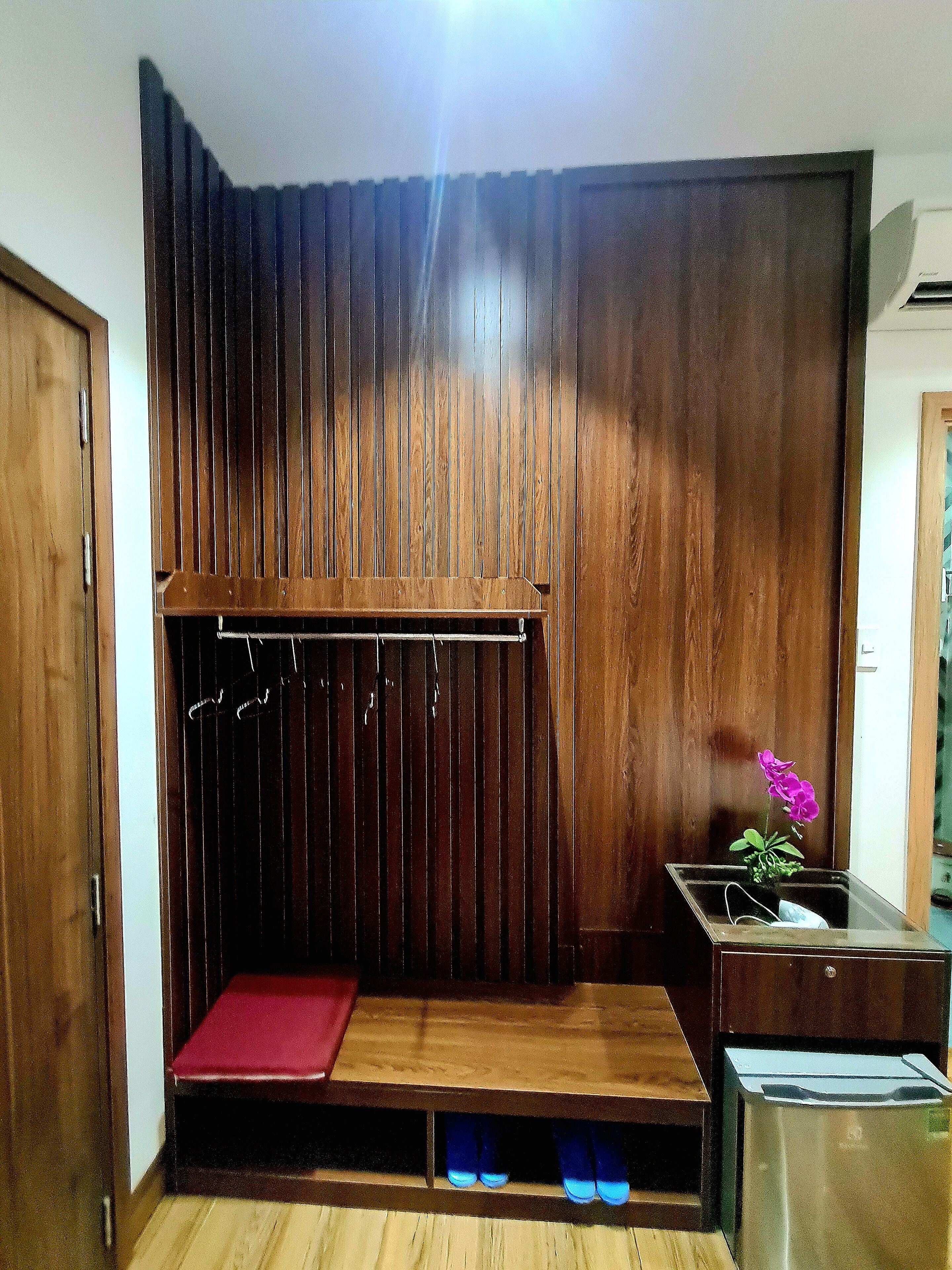 A room with a wooden slatted wall, a small bench, a shoe rack, and a trash bin.
