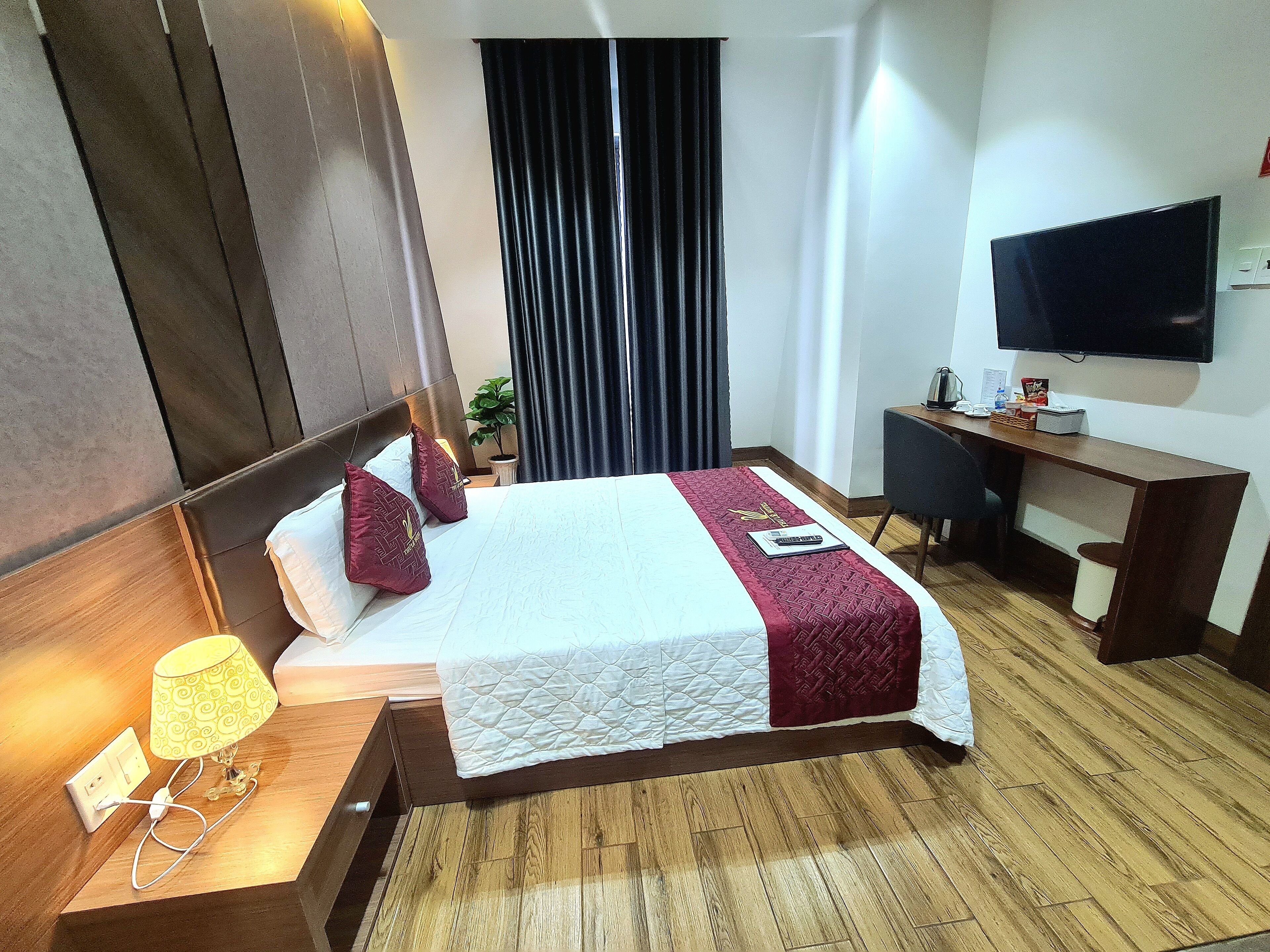 Una habitación de hotel con cama, escritorio, televisor y ventana con cortinas.