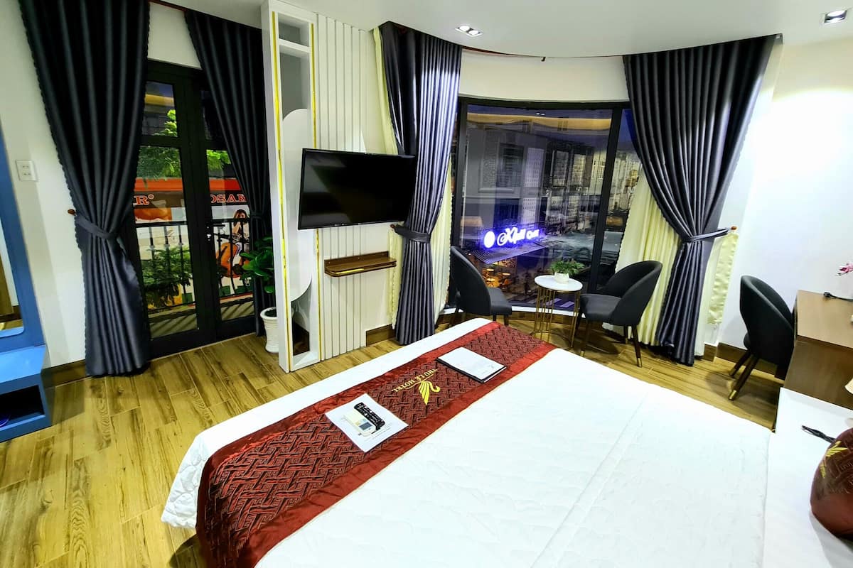 Quarto de hotel com cama, televisão, escrivaninha e vista para a cidade.