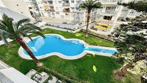 Un quartier résidentiel doté d’une piscine entourée de pelouse et de palmiers.