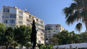 Un immeuble à plusieurs étages doté de balcons, entouré de palmiers et surmonté d’une pergola blanche.