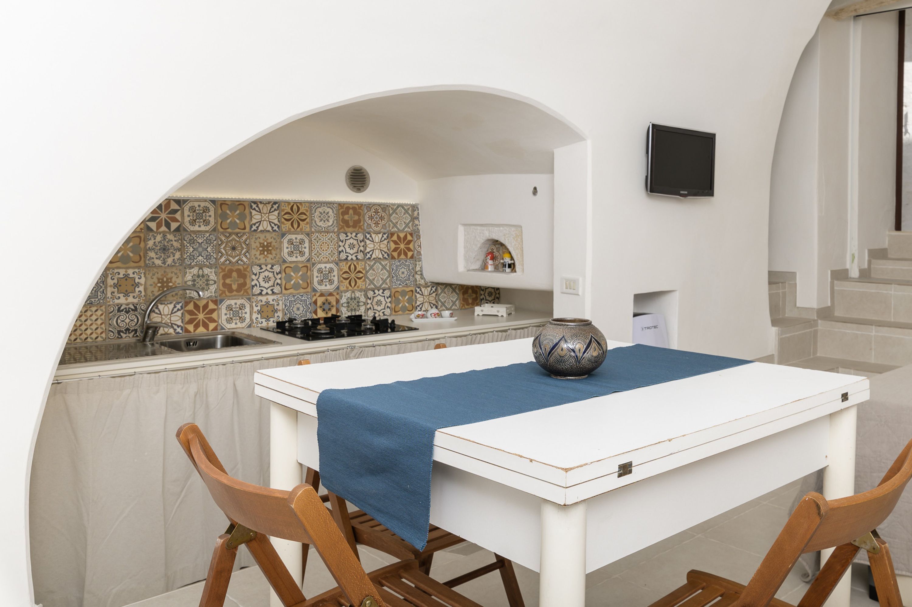 Une cuisine de taille réduite avec un mur recouvert de carreaux, un plan de travail blanc et une nappe bleue.