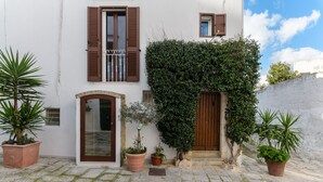 Un edificio bianco con persiane marroni, un ingresso in pietra e piante in vaso.