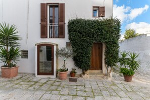 Un bâtiment blanc avec des volets bruns, une entrée en pierre et des plantes en pot.
