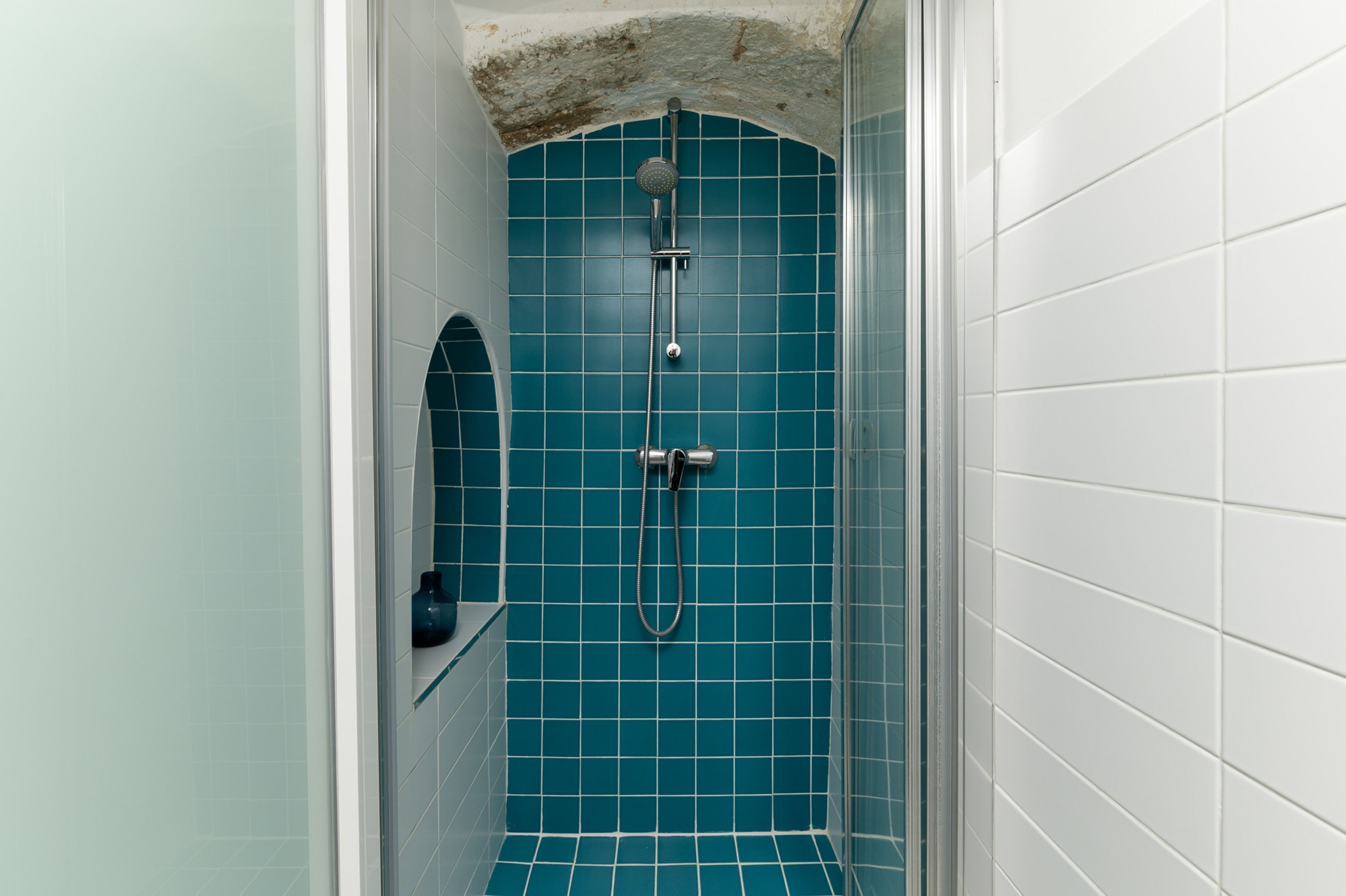 A small, enclosed shower area with blue tiles and a white tiled wall.